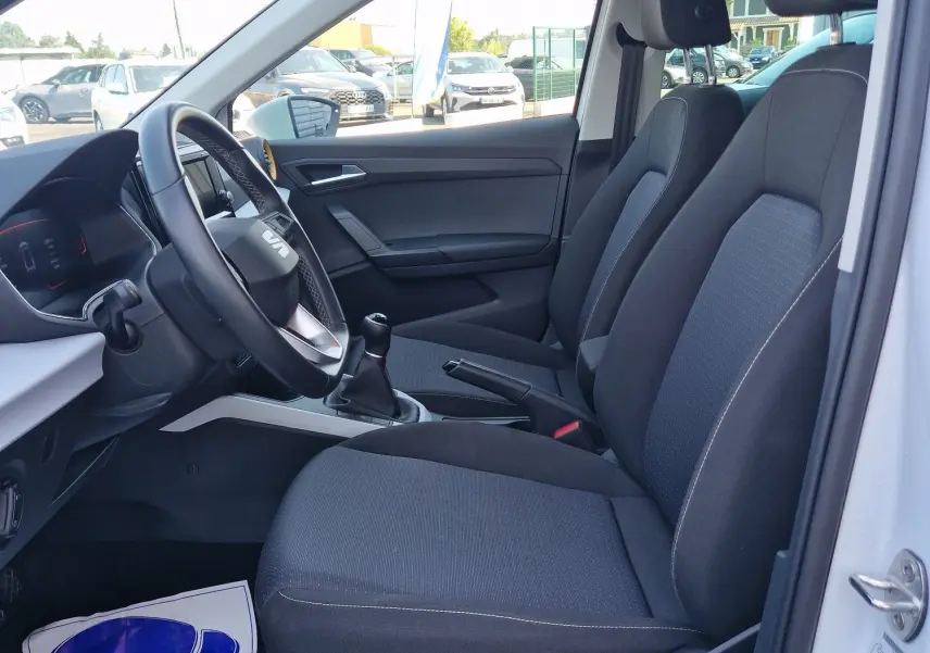 Vue intérieure côté conducteur du SEAT Arona blanc alpin avec sièges tissu noirs et volant cuir multifonction.