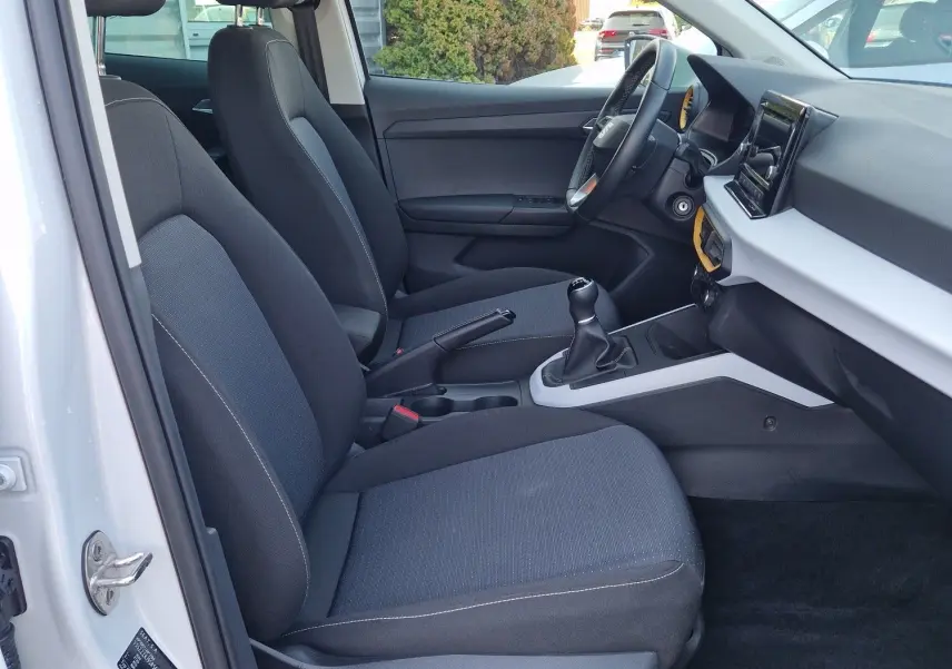 Intérieur côté conducteur du SEAT Arona blanc, montrant les sièges tissu noirs et la console centrale avec boîte manuelle.