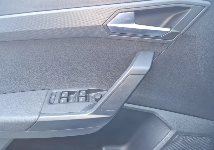 Vue intérieure côté gauche de la porte d’un SEAT Arona 2025, avec commandes de vitres et poignée noire.
