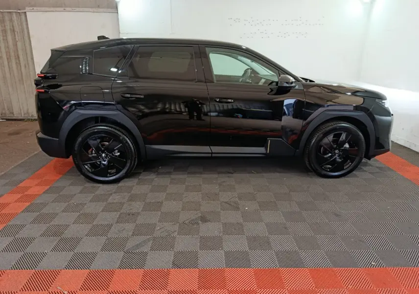 Vue latérale gauche d'une Citroën C5 hybride noire avec jantes noires, dans un garage éclairé.