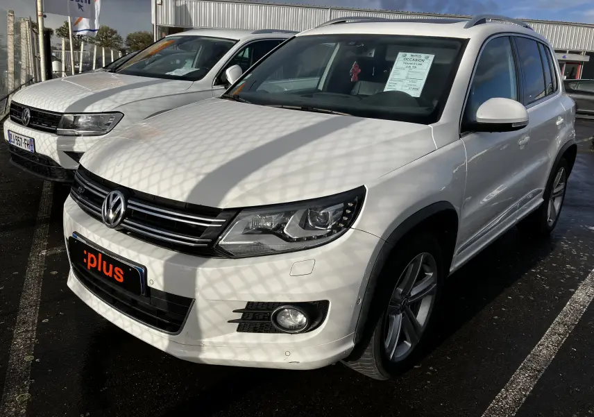 Volkswagen Tiguan blanc en 3/4 avant droit, avec calandre rline et jantes alliage visibles sous un ciel partiellement nuageux.