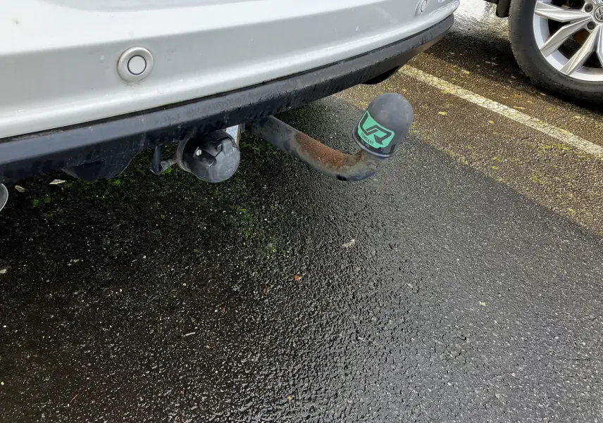 Gros plan sur l'attelage arrière rouillé d'un Volkswagen Tiguan blanc, avec capuchon de protection vert et noir.