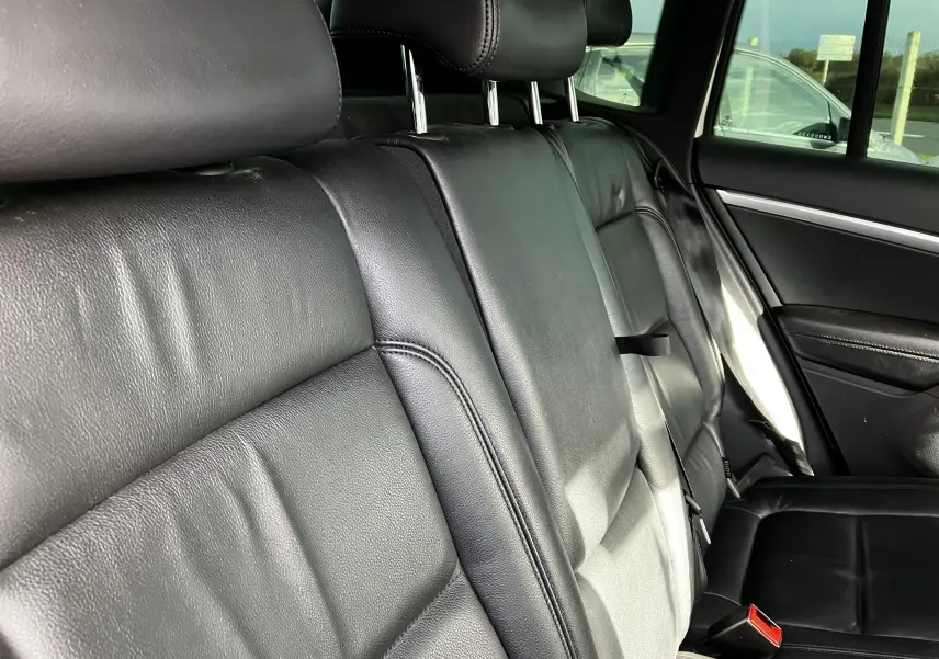 Vue rapprochée des sièges arrière en cuir noir du Volkswagen Tiguan blanc, avec appuie-têtes et ceintures visibles.