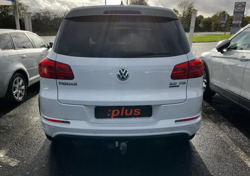 Vue arrière d'un Volkswagen Tiguan blanc 2.0 TDI avec logo et badges visibles sur un parking extérieur.