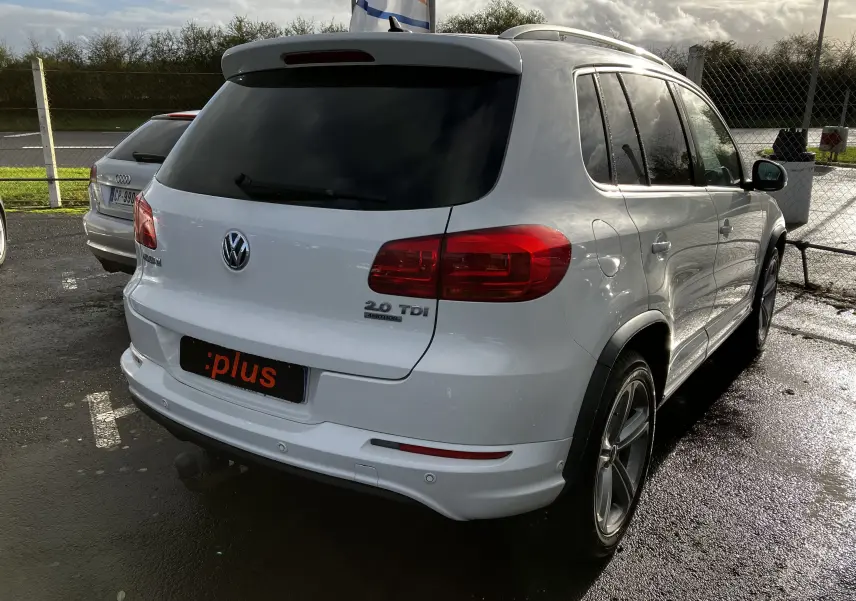 Volkswagen Tiguan blanc vu en 3/4 arrière droit avec badges 2.0 TDI et 4MOTION sur un parking humide.
