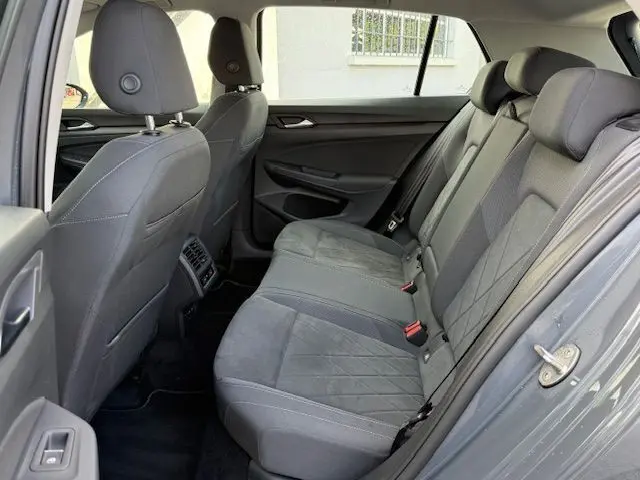 Vue intérieure arrière côté droit de la Volkswagen Golf VIII gris dauphin, montrant les sièges arrière en tissu gris et les appuie-têtes.