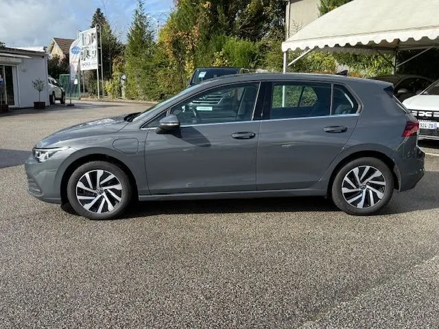 Profil côté gauche d'une Volkswagen Golf VIII 1.4 e-Hybrid gris dauphin, avec jantes alliage et portes fermées.