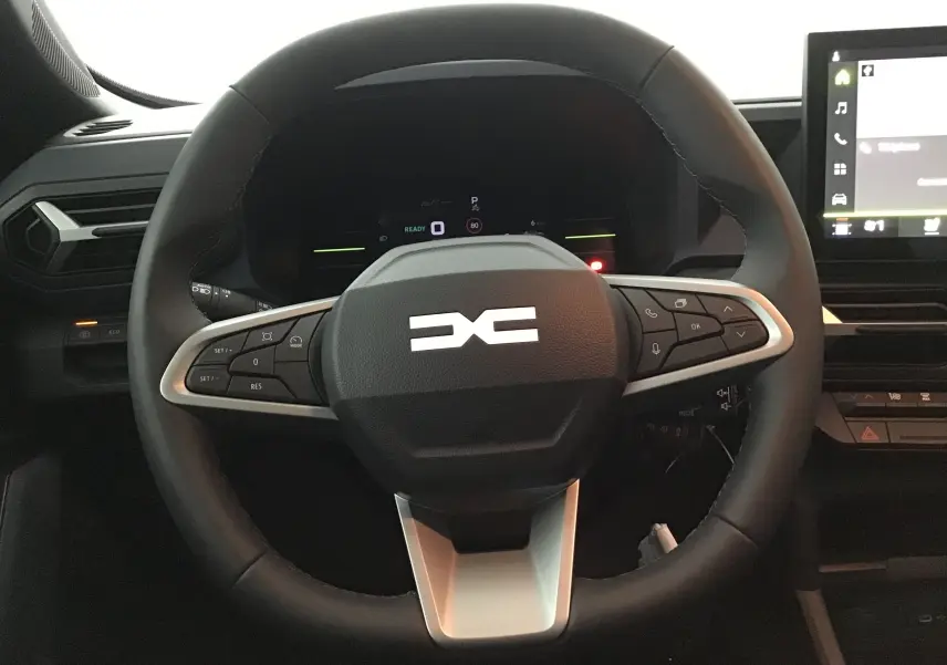 Vue rapprochée du volant multifonctions noir du Dacia Duster 2025 avec tableau de bord numérique et écran tactile.