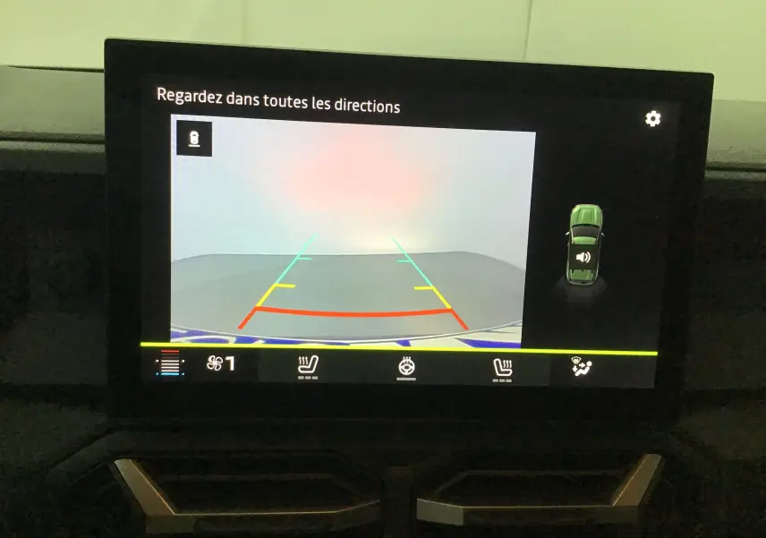 Écran intérieur du Dacia Duster 2025 montrant la caméra de recul avec lignes de guidage colorées et affichage des commandes de sièges chauffants.