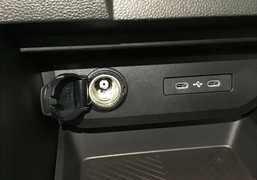 Prise allume-cigare ouverte et deux ports USB-C visibles sur la console centrale du Dacia Duster blanc glacier 2025.