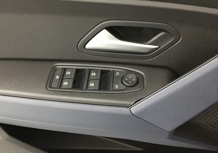 Gros plan sur la commande des vitres et le bouton de réglage des rétroviseurs côté conducteur du Dacia Duster blanc glacier 2025.
