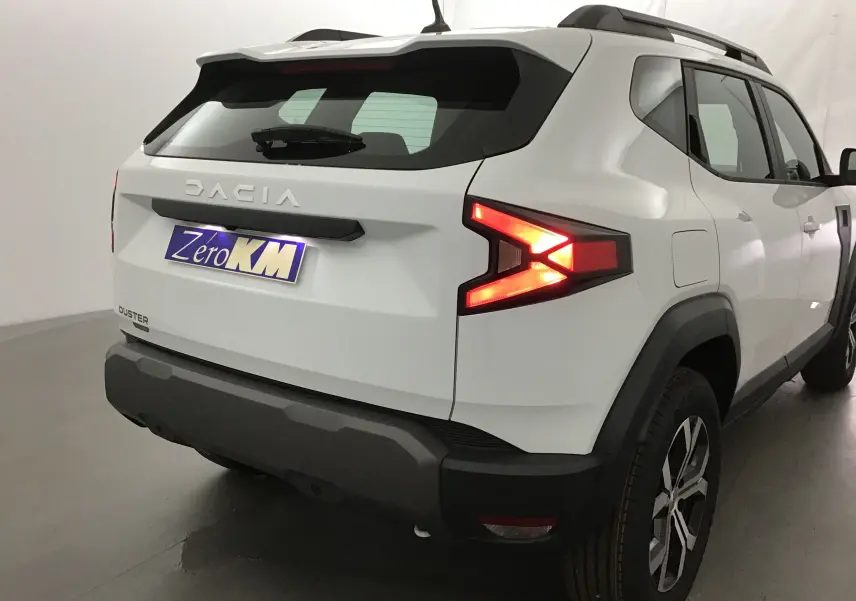 Vue 3/4 arrière droite du Dacia Duster blanc glacier 2025 avec feux arrière allumés et jantes alliage.