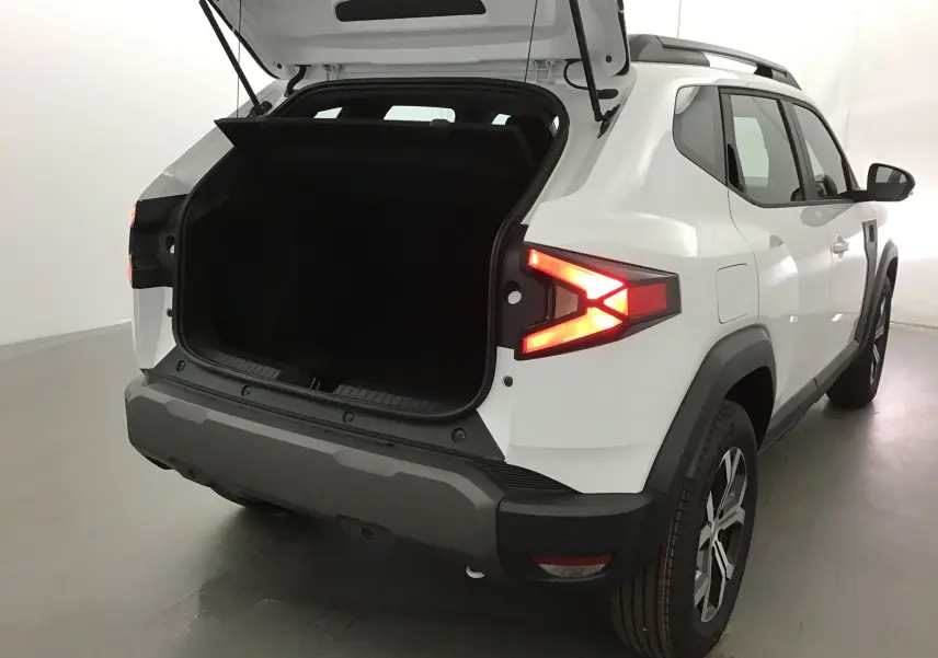 Vue arrière droite du Dacia Duster blanc glacier 2025 avec coffre ouvert et feux arrière allumés.