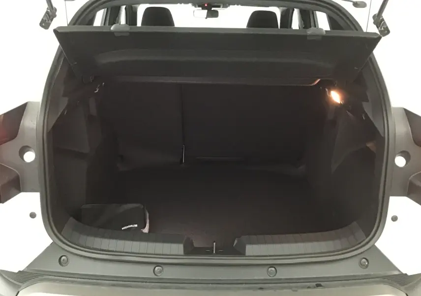 Coffre ouvert vu de l'arrière du Dacia Duster blanc glacier 2025, intérieur noir avec éclairage latéral allumé.