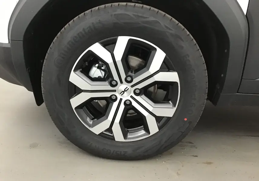 Gros plan sur la roue avant gauche du Dacia Duster blanc glacier 2025, mettant en valeur la jante alliage noire et argentée.