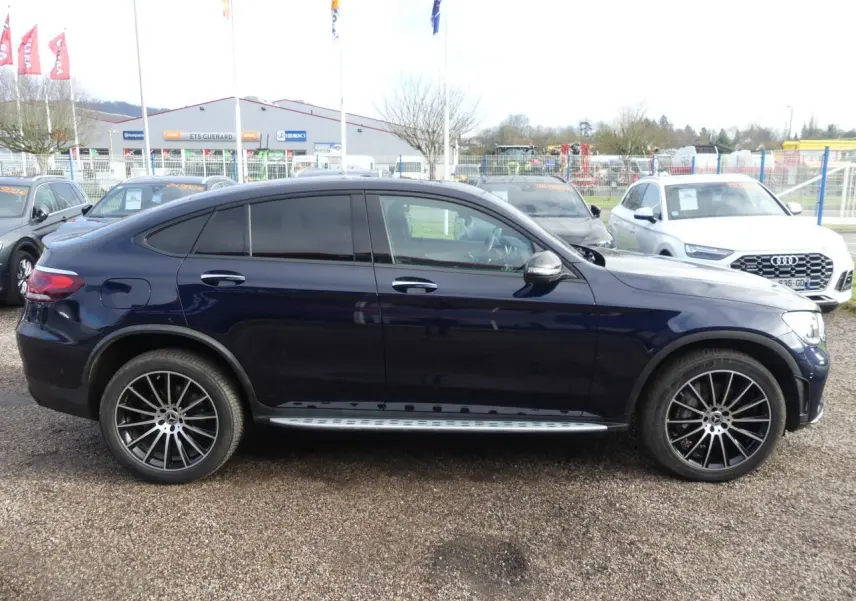 Profil côté gauche d'un Mercedes GLC Coupé 300 hybride bleu foncé avec jantes AMG noires brillantes et marchepieds acier.