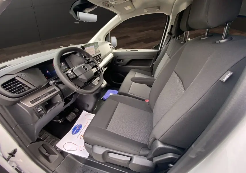 Vue intérieure côté conducteur de l'Opel Vivaro blanc 2025, montrant le tableau de bord et les sièges noirs en tissu.