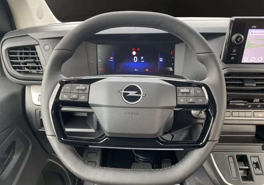 Volant noir de l'Opel Vivaro 2025 avec commandes intégrées et tableau de bord numérique visible en arrière-plan.