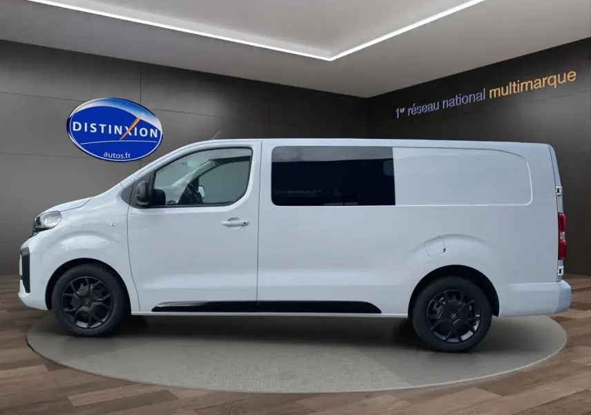 Profil droit d'un Opel Vivaro blanc 2025 avec vitres teintées et jantes noires en intérieur showroom.