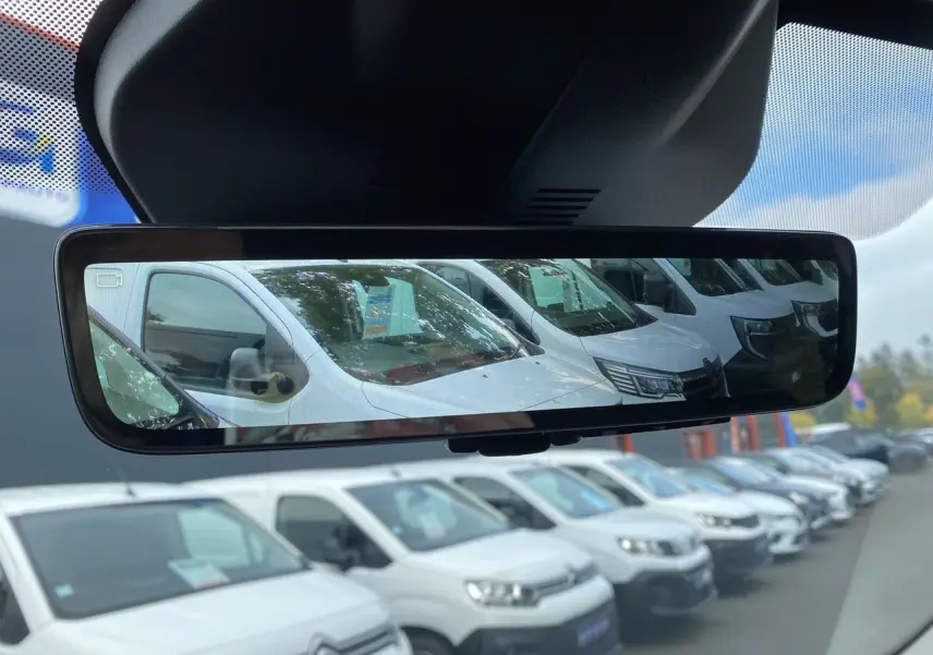 Rétroviseur intérieur montrant plusieurs fourgons blancs en stationnement, dont un Opel Vivaro blanc en 3/4 avant.