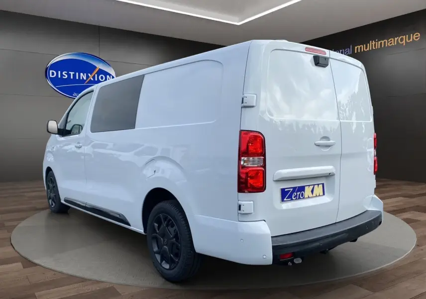 Vue 3/4 arrière droite d'un utilitaire Opel Vivaro blanc avec attelage et jantes noires en showroom.