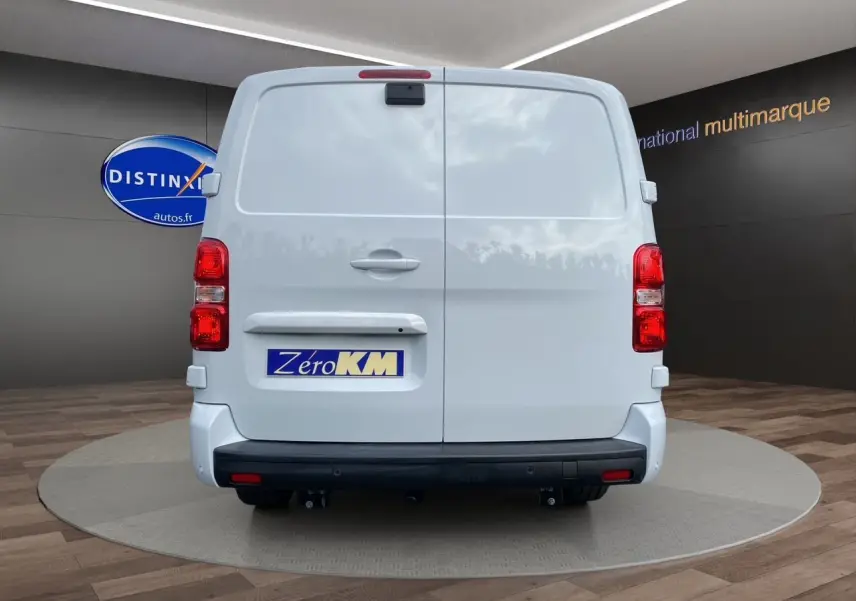 Vue arrière d’un utilitaire Opel Vivaro blanc avec attelage et plaque Zéro KM dans un showroom.