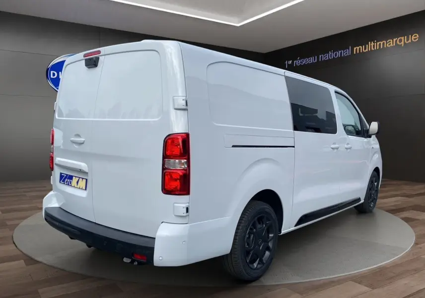 Vue 3/4 arrière droite d'un Opel Vivaro blanc avec jantes noires et attelage démontable en showroom.