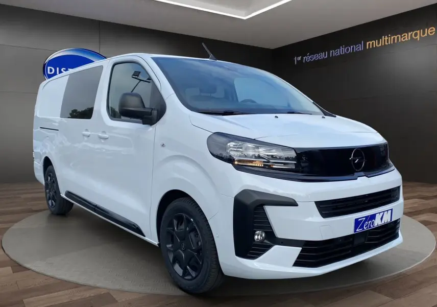 Opel Vivaro blanc vu en 3/4 avant droit, avec calandre noire et jantes foncées dans un showroom.