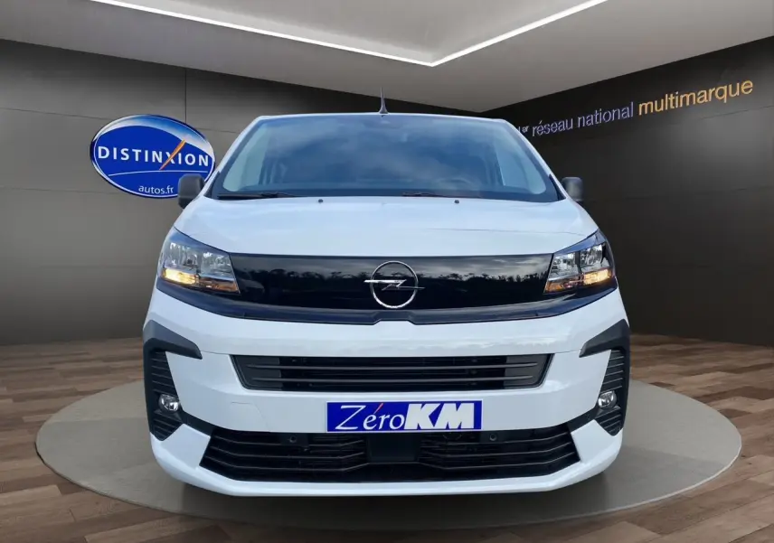 Vue frontale d'un Opel Vivaro blanc avec calandre noire et feux allumés en showroom.