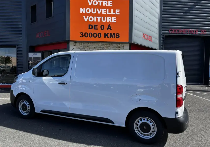 Peugeot Expert Fourgon blanc vu de profil côté gauche, stationné devant un bâtiment commercial.