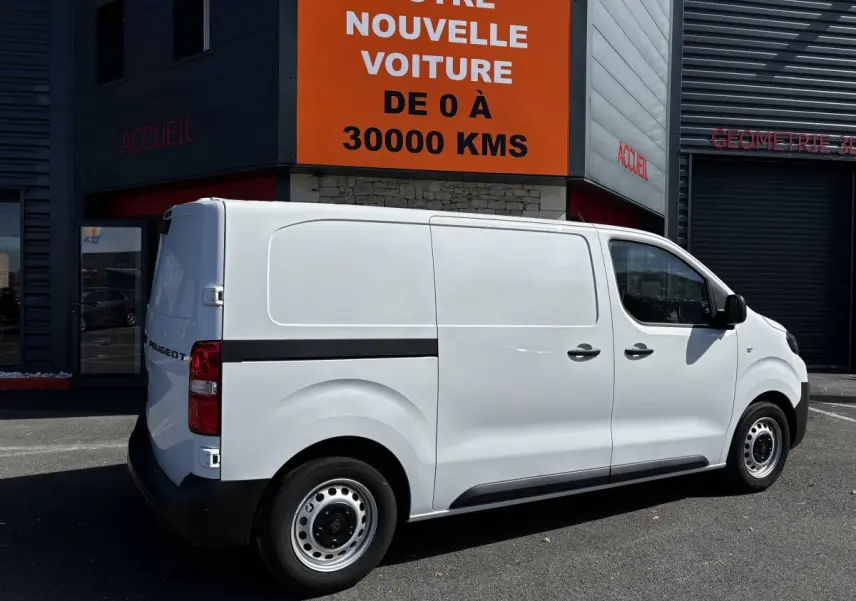 Peugeot Expert Fourgon blanc vu de profil côté droit, stationné devant un bâtiment commercial.