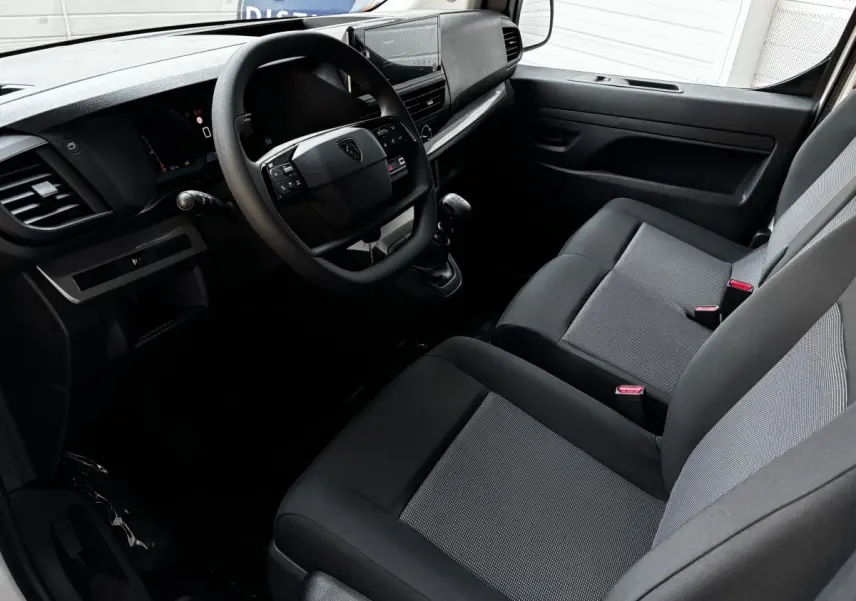 Intérieur du Peugeot Expert Fourgon 2025 vu côté conducteur, montrant le tableau de bord et sièges gris foncé avec tissu clair.