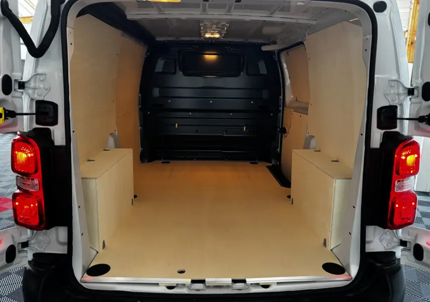 Vue arrière du Peugeot Expert Fourgon blanc 2025 avec intérieur de chargement en bois clair et éclairage intérieur allumé.