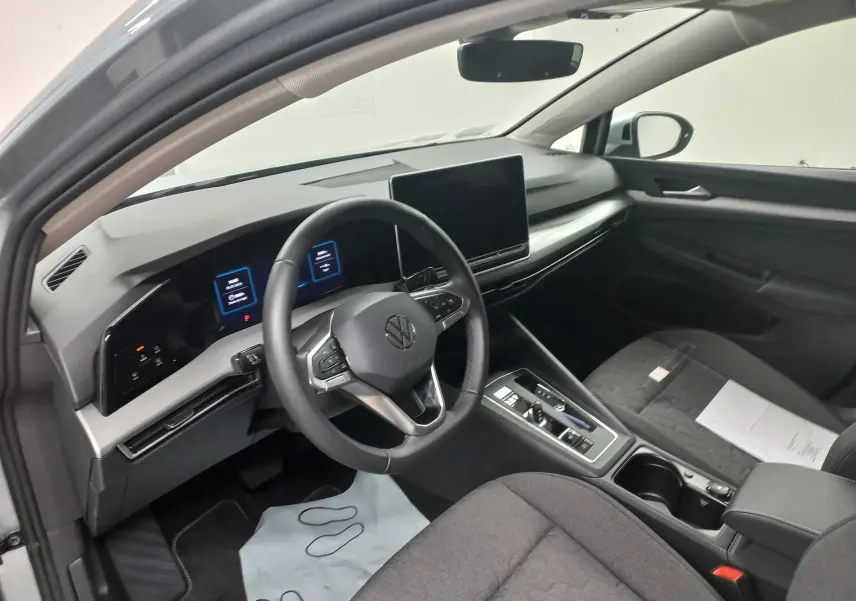 Vue intérieure côté conducteur de la Volkswagen Golf 1.5 eHybrid 2025, tableau de bord numérique et écran tactile central.
