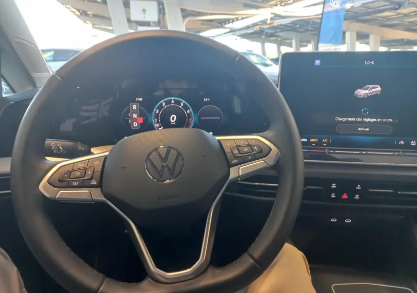 Vue intérieure centrée sur le volant Volkswagen d'une Golf 1.5 eHybrid 2025 avec tableau de bord numérique et écran tactile.