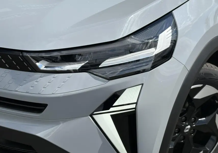 Gros plan sur le phare avant droit et la jante noire du Renault Captur Gris Rafale 2025 en hybride.