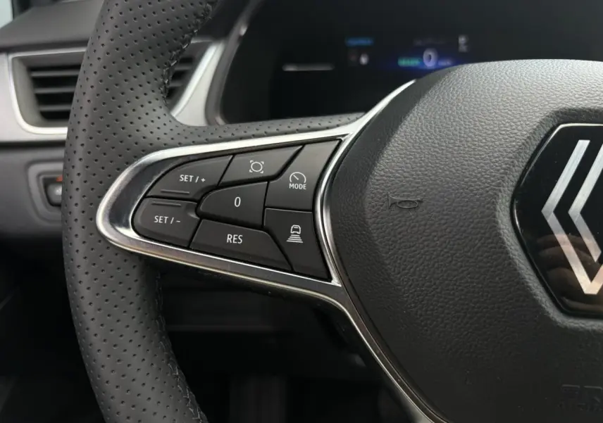 Gros plan sur les commandes du volant à gauche du Renault Captur gris Rafale, mettant en valeur les boutons du régulateur adaptatif.