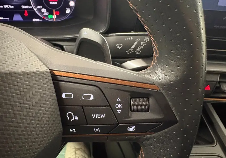 Gros plan sur le volant perforé avec commandes intégrées du CUPRA Formentor gris Graphène, tableau de bord numérique en arrière-plan.