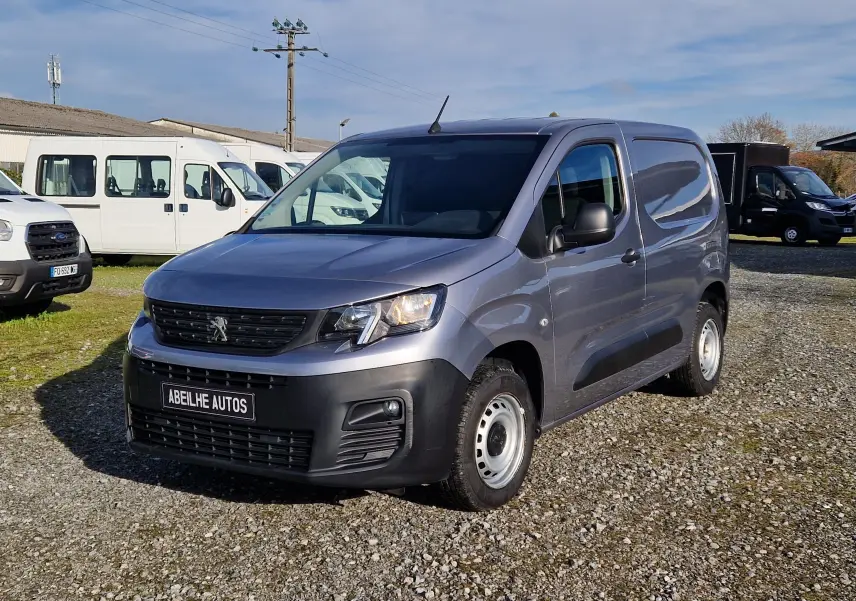 Peugeot Partner gris Artense vu en 3/4 avant droit, fourgonnette utilitaire avec calandre noire et jantes acier.