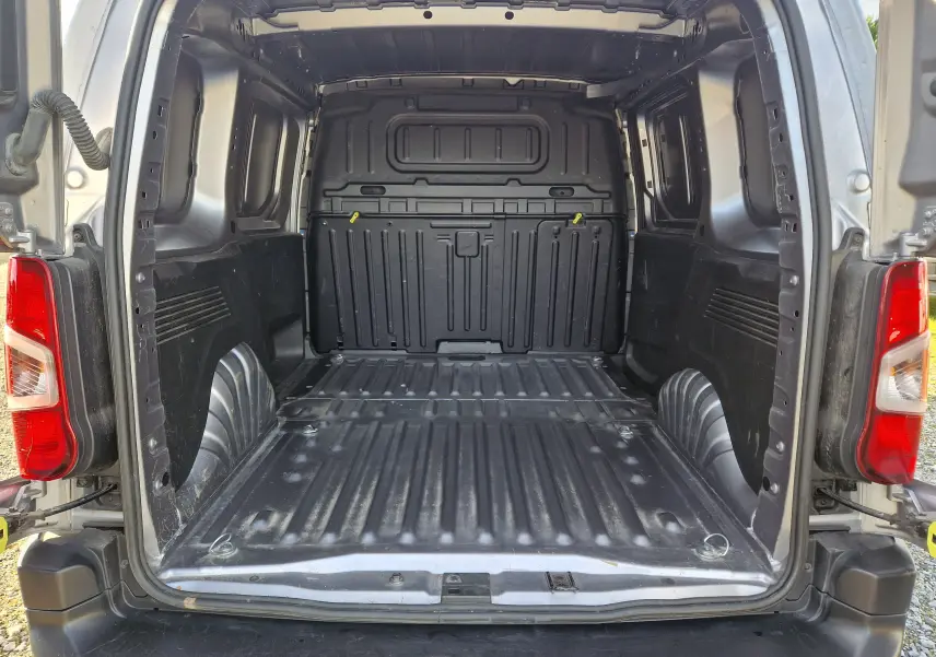 Vue arrière ouverte du fourgon Peugeot Partner gris Artense, montrant l'espace de chargement vide et les feux arrière rouges.