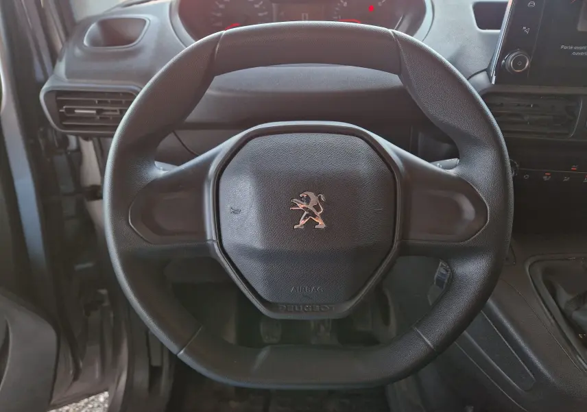 Gros plan sur le volant noir du Peugeot Partner 2021, avec logo lion au centre et tableau de bord en arrière-plan.