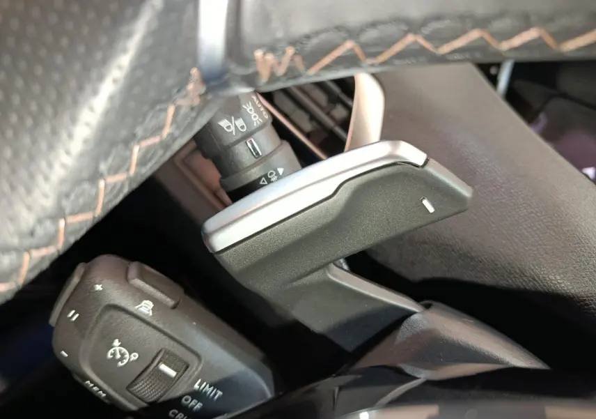 Gros plan sur la commande de régulateur de vitesse et palettes au volant cuir noir du Peugeot 5008 GT bleu 2023.