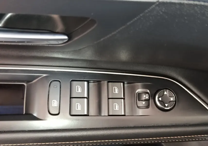 Gros plan sur les commandes de lève-vitres et rétroviseurs côté gauche intérieur d’un Peugeot 5008 bleu 2023.