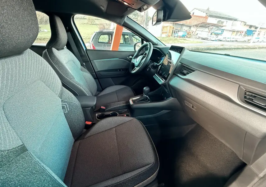 Intérieur avant du Renault Captur E-Tech hybride 2025, sièges noirs et tableau de bord avec écran tactile vertical.