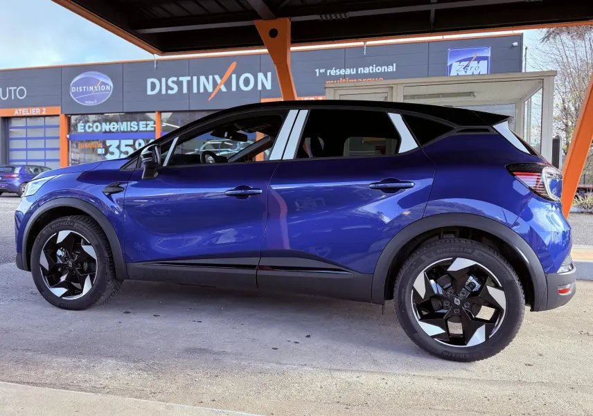 Profil côté gauche du Renault Captur E-Tech F.Hybrid 145ch 2025 en bleu Iron Metal avec toit noir et jantes noires distinctives.