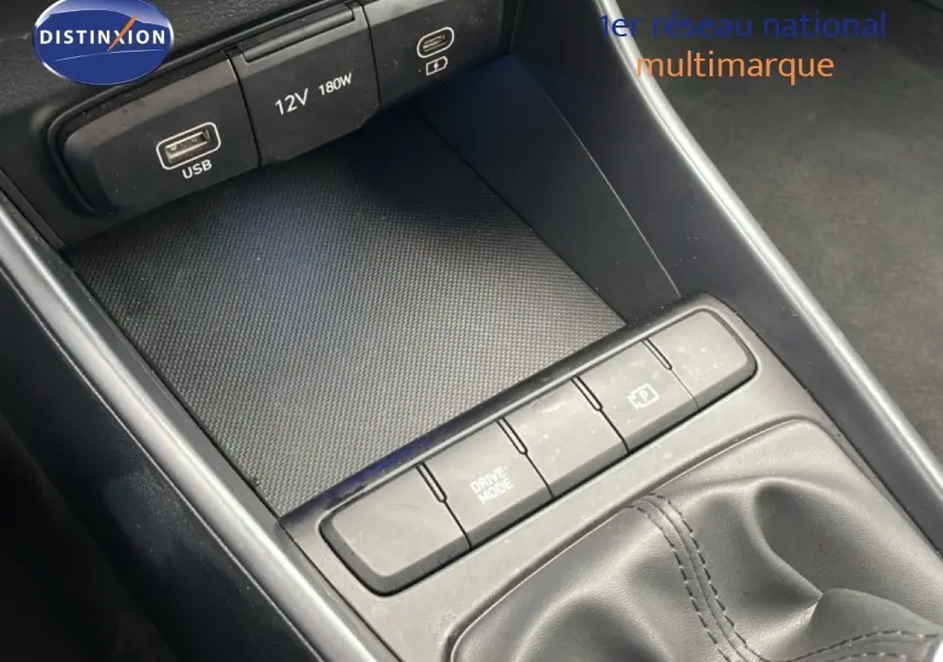 Gros plan sur la console centrale noire de la Hyundai i20 2025, montrant les ports USB, prise 12V et boutons de commande près du levier de vitesses.