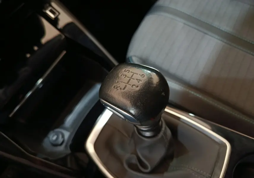 Gros plan sur le levier de vitesses manuel noir et la sellerie grise à motifs de la Peugeot 208 PureTech 100 S&S Allure Business.
