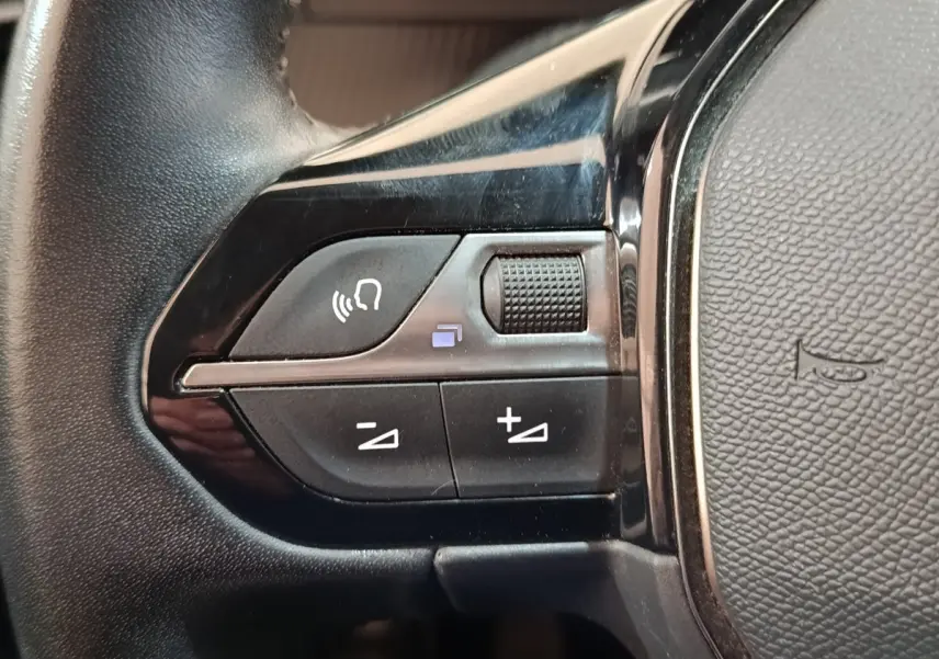 Gros plan sur les commandes gauche du volant noir de la Peugeot 208 PureTech 100 S&S Allure Business 2021.
