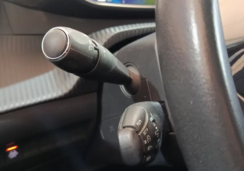 Gros plan sur la colonne de direction et commandes au volant d'une Peugeot 208 blanche, intérieur noir.
