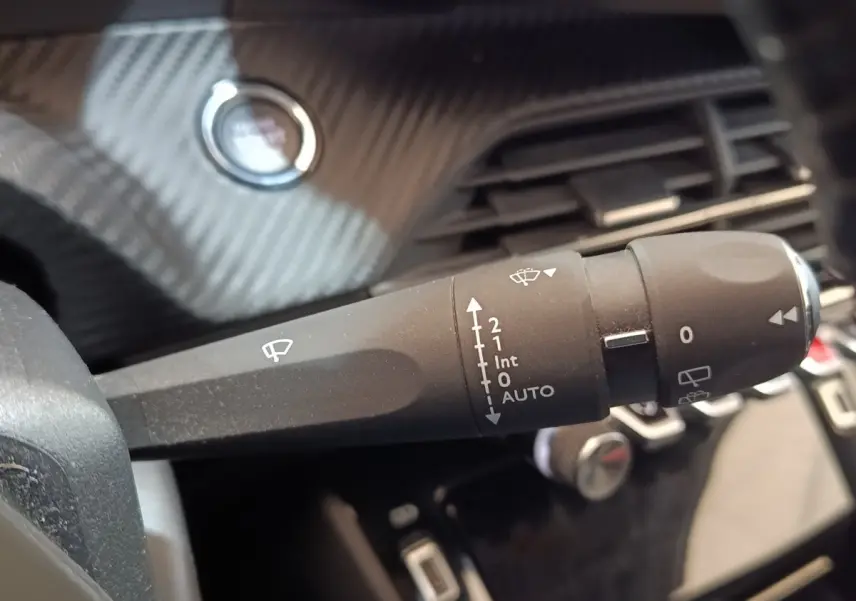Gros plan sur la commande des essuie-glaces dans l’habitacle du Peugeot 208 blanc, avec bouton démarrage en arrière-plan.